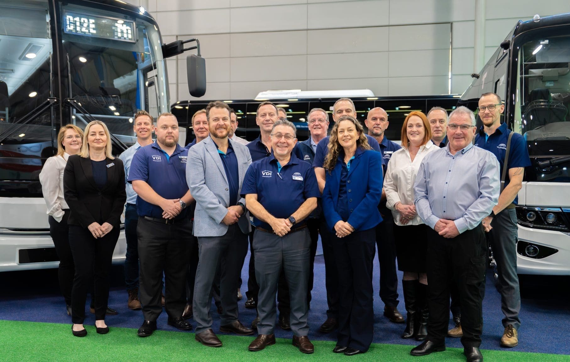 VDI Australia team standing together at the Brisbane Bus and Coach Show 2024, with Yutong zero-emission buses in the background.